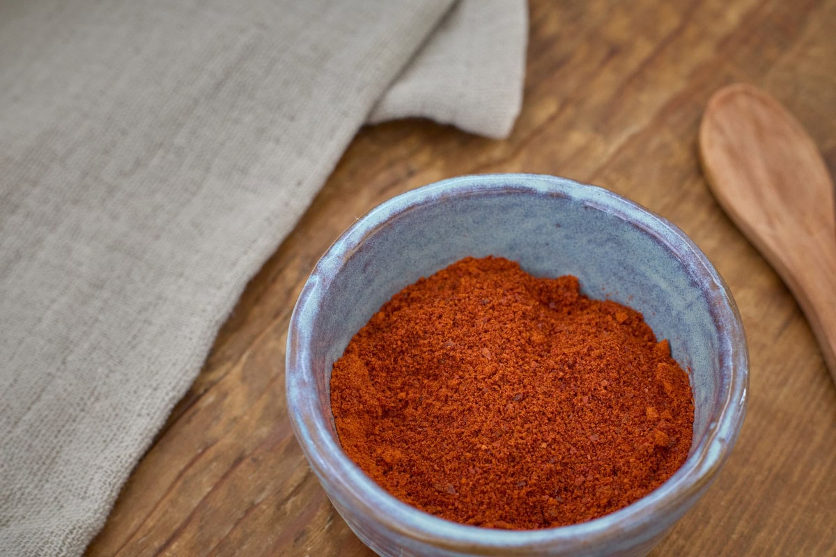 szeged paprika pepper powder in a small bowl with a spoon and a kitchen towel alongside