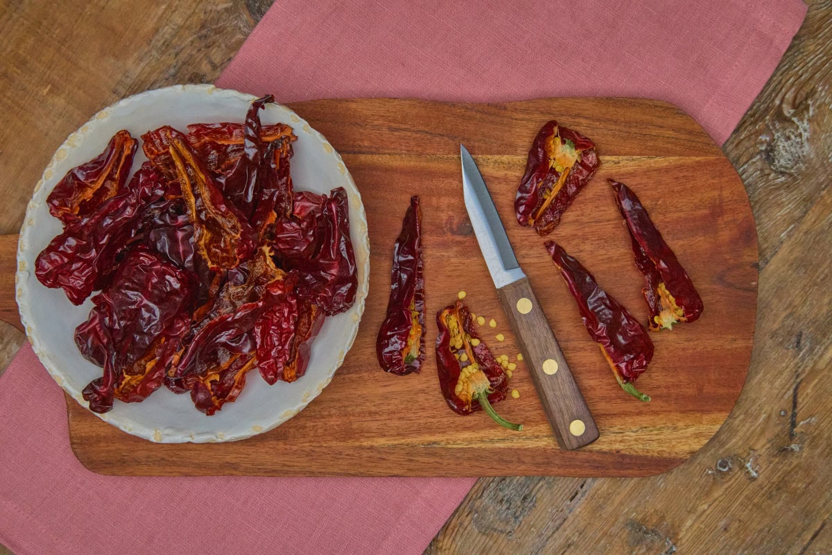 pieces of dried leutschauer paprika peppers in a bowl and on a cutting board with a paring knife atop a napkin on a rustic wooden table