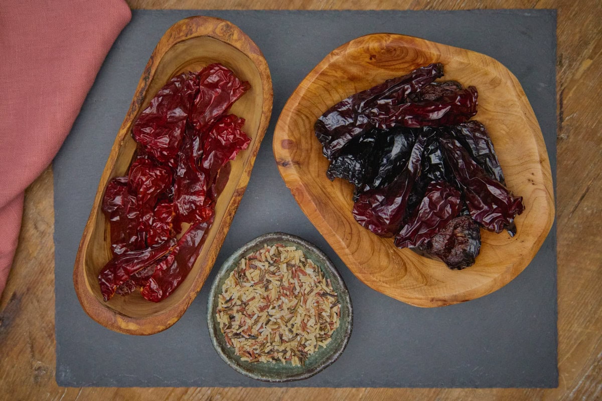 unsmoked and smoked leutschauer paprika peppers in bowls and dried rice in a bowl atop a stone tray with a napkin alongside