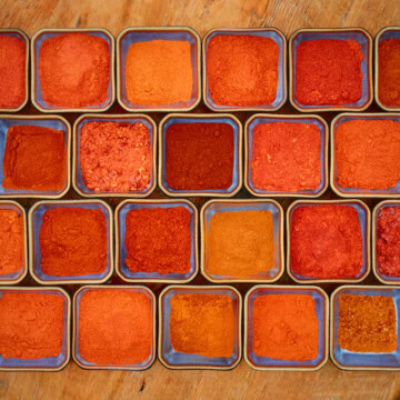 a variety of pepper powders in small blue square bowls on a rustic wooden table