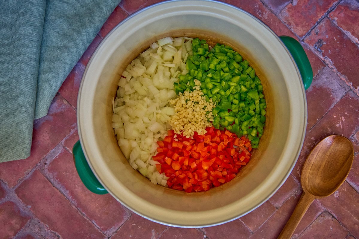 a pot with onions, peppers, and garlic, with a mixing spoon and napkin in the background