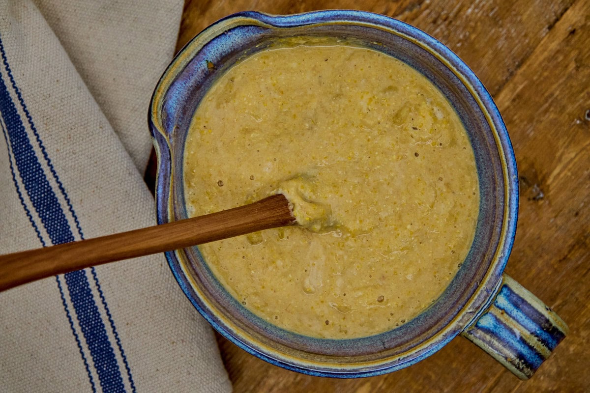 banana cornbread ingredients mixed together with a wooden mixing spoon in a mixing bowl with a kitchen towel on the side