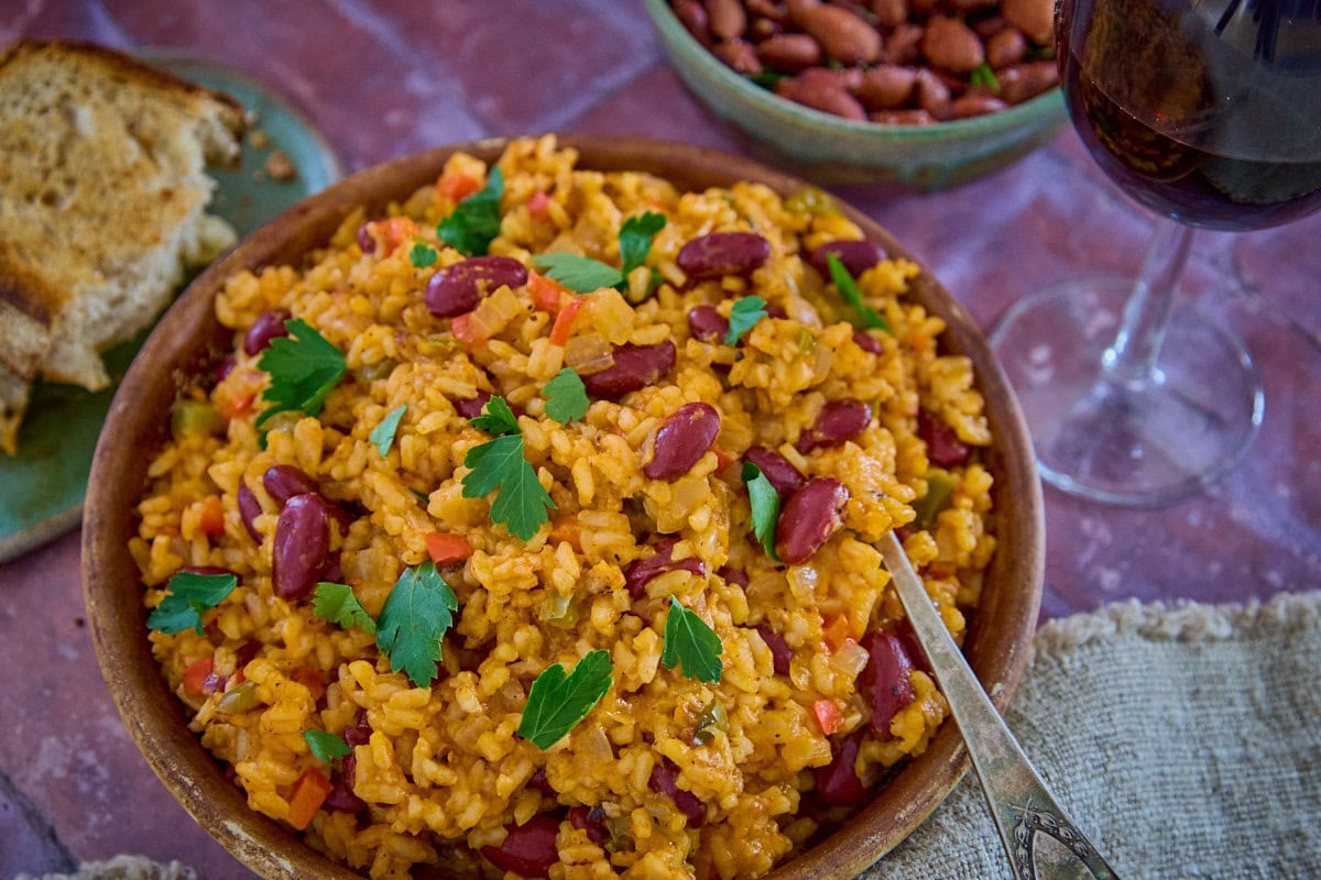 a bowl of beans and rice with a piece of bread, almonds, paprika, a glass of wine, and a napkin in the background