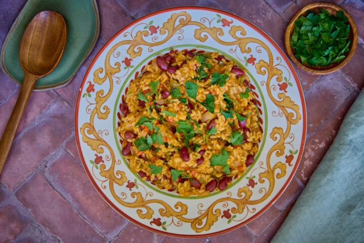 a bowl of finished Arroz de Feijão, parsley, a mixing spoon, and a napkin in the background