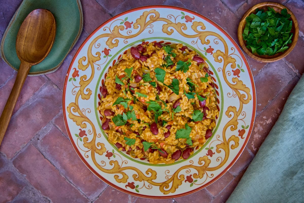 a bowl of finished Arroz de Feijão, parsley, a mixing spoon, and a napkin in the background