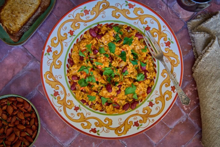 a bowl of beans and rice with a piece of bread, almonds, a glass of wine, a napkin, and a fork in the background