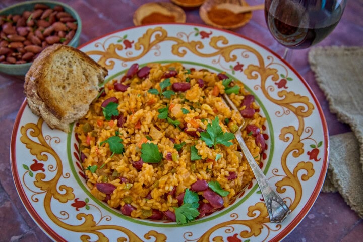 a bowl of beans and rice with a piece of bread, almonds, paprika, a glass of wine, a napkin, and a fork in the background