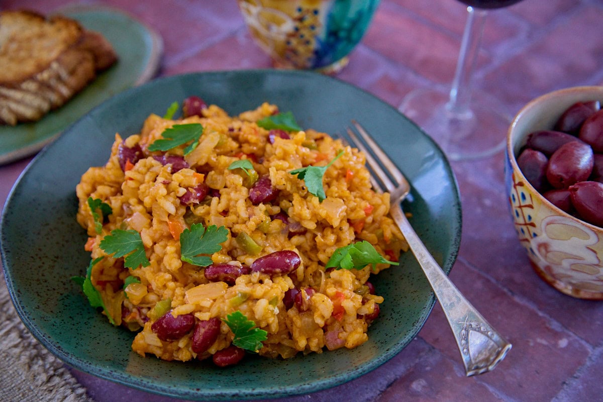 a bowl of beans and rice with a piece of bread, a glass of wine, a napkin, and a fork in the background