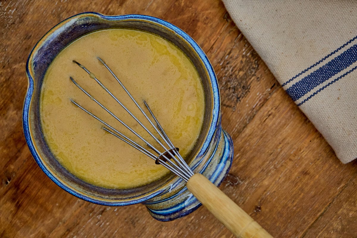 wet ingredients in a mixing bowl with a whisk, and a kitchen towel alongside