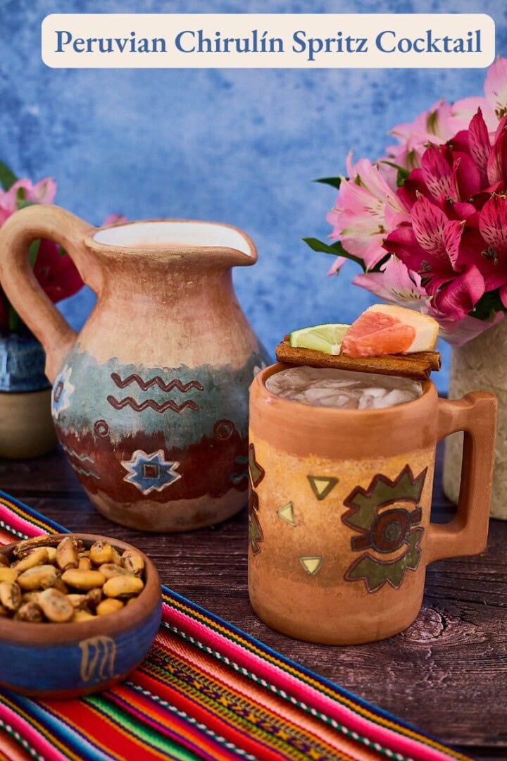 a labeled photo of a Peruvian clay mug and pitcher of chirulin spritz cocktail with vases of flowers, toasted corn, and a piece of fabric around them