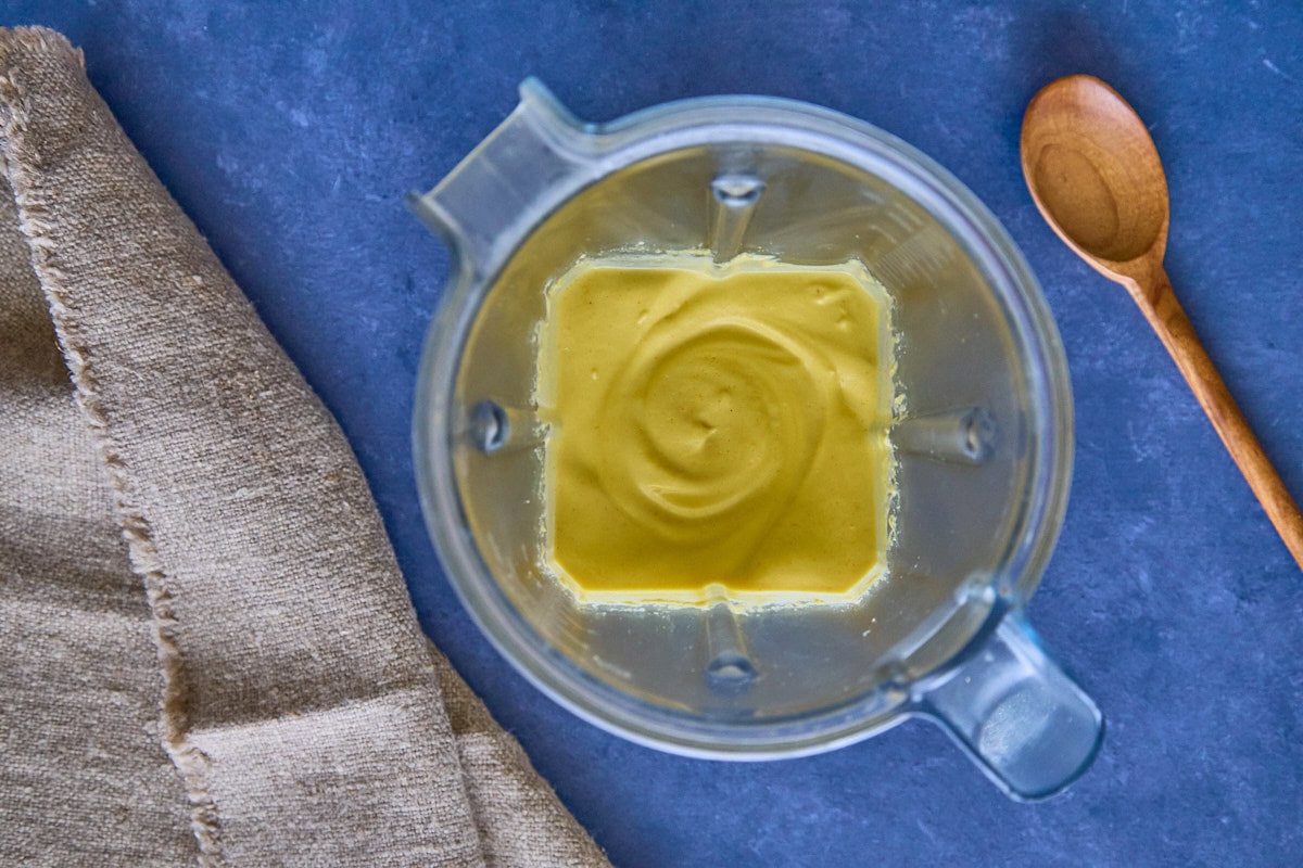 blended huancaína sauce ingredients in a blender, with a napkin and wooden mixing spoon alongside