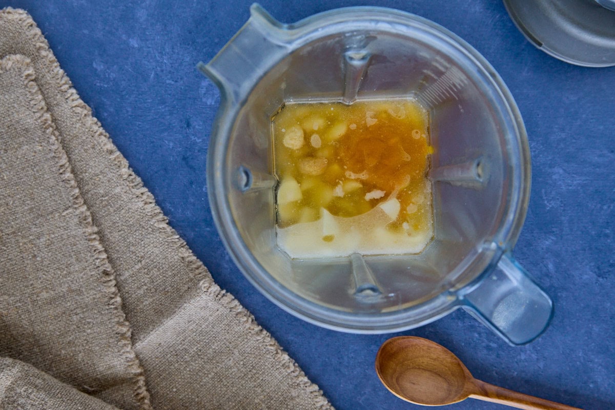 unblended huancaína sauce ingredients in a blender, with a napkin, wooden mixing spoon, and blender top alongside