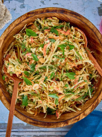 wooden bowl of salad with wooden utensils, basket of crispbread, jar of pickled onions, and napkin