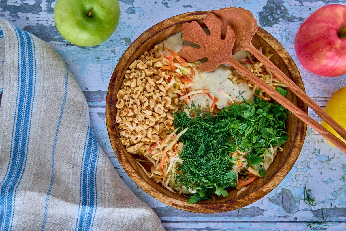a bowl of unmixed salad ingredients and serving utensils, kitchen towel, apples, and lemon