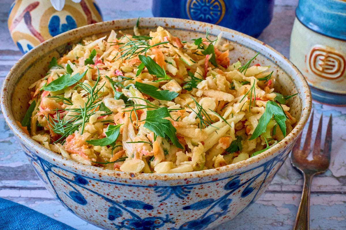 a bowl of parsnip salad with a fork and napkin, vases of daisies, and cup of coffee