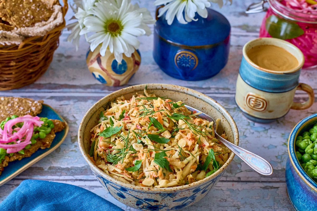 a bowl of salad with a fork and napkin, plate of crispbread topped with peas and onions, basket of crispbread, vases of daisies, jar of pickled onions, cup of coffee, and bowl of peas