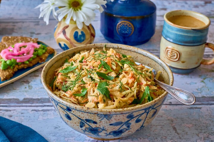 a bowl of salad with a fork and napkin, plate of crispbread topped with peas and onions, vases of daisies, and cup of coffee