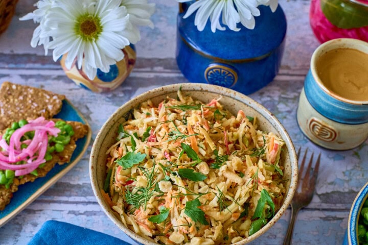 a bowl of salad with a fork and napkin, plate of crispbread topped with peas and onions, vases of daisies, jar of pickled onions, cup of coffee, and bowl of peas