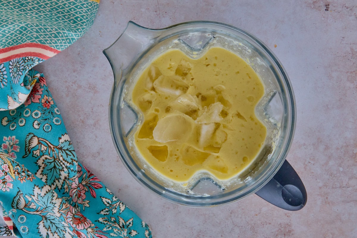 blended cocktail ingredients and ice in a blender with a kitchen towel in the background