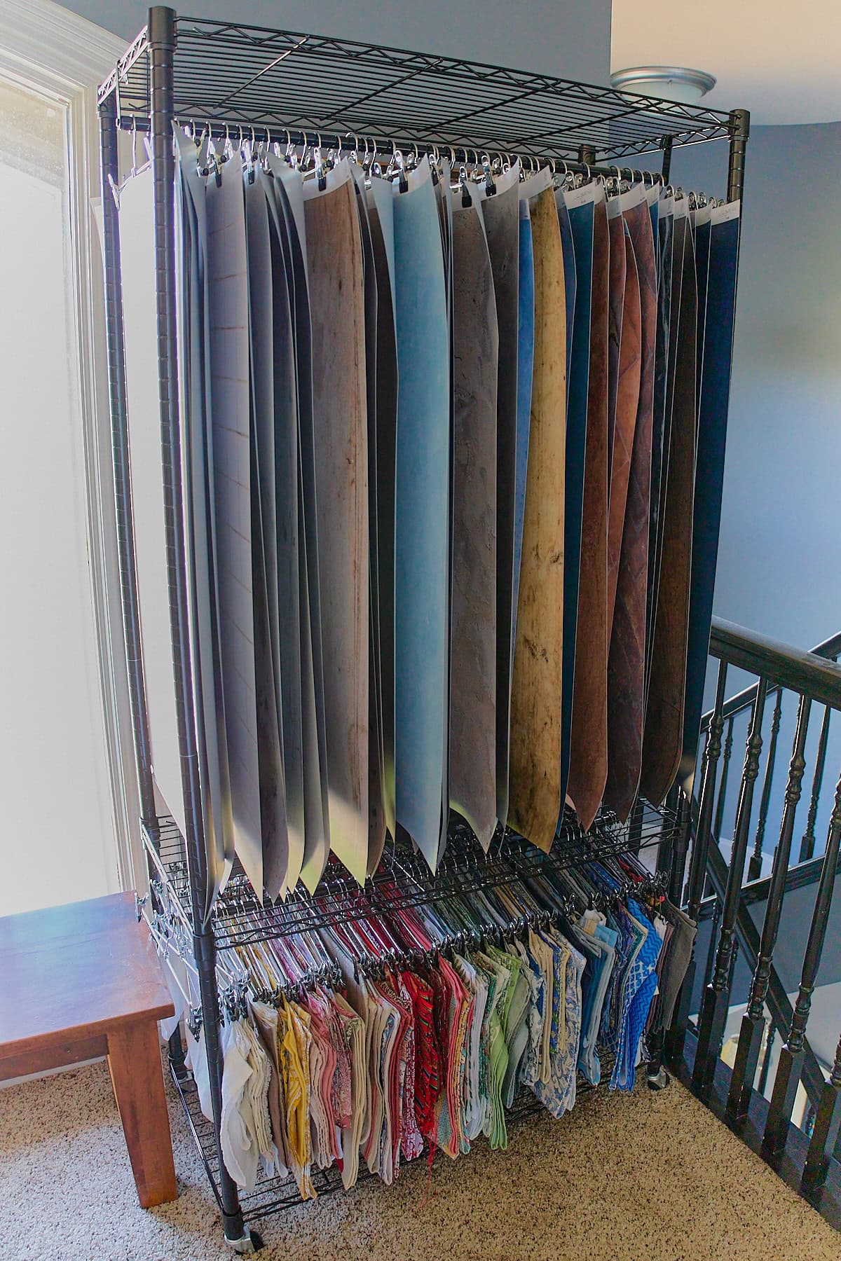 a shelving unit with vertically hanging photography backdrops on the top rack and napkins and kitchen towels on the bottom rack