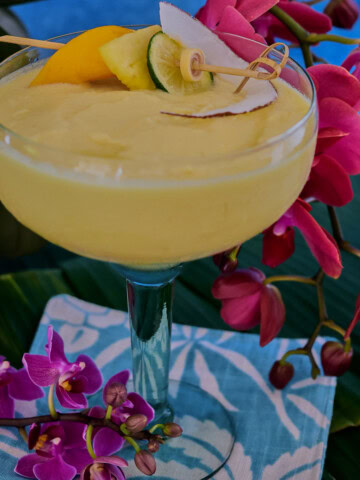 a cocktail in a glass on banana leaves on a cocktail napkin with orchids in the background