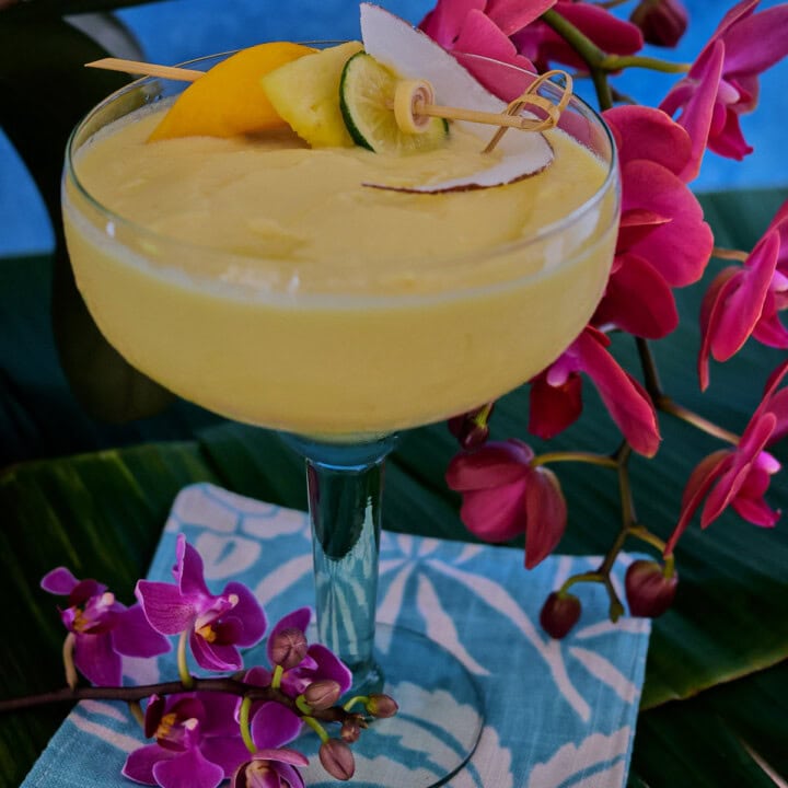 a cocktail in a glass on banana leaves on a cocktail napkin with orchids in the background