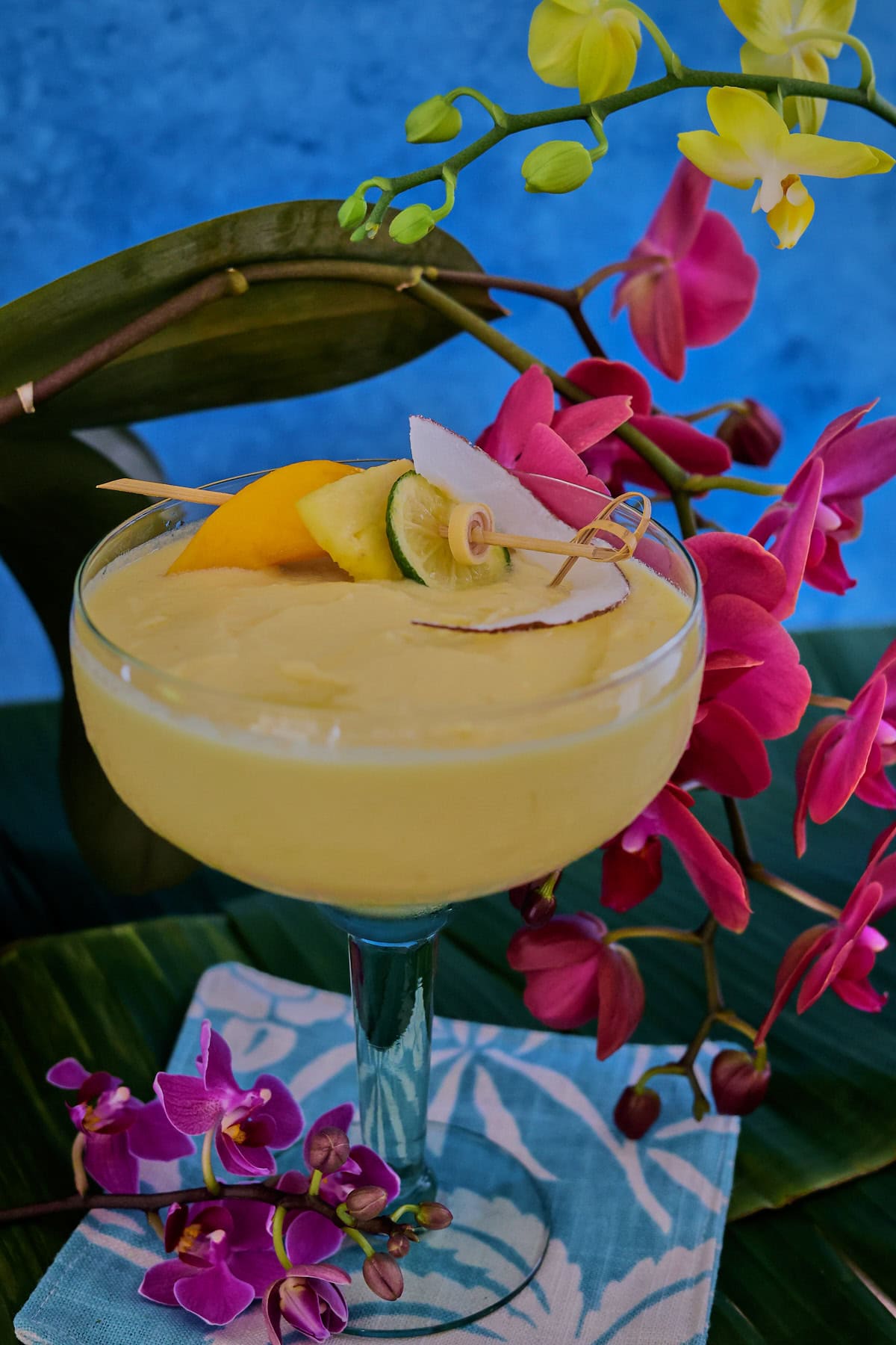 a cocktail in a glass on banana leaves on a cocktail napkin with orchids in the background