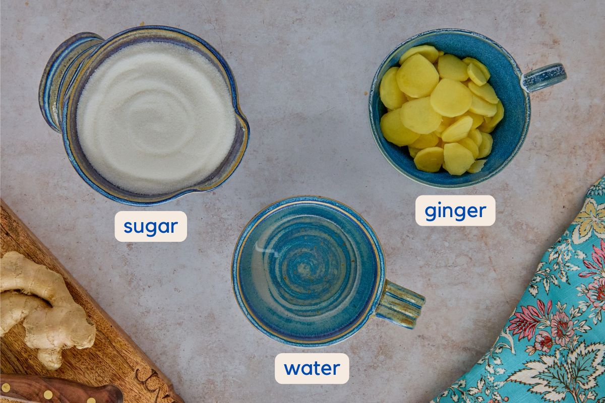 labeled ingredients for ginger syrup, a kitchen towel, and a cutting board with a knife and ginger root