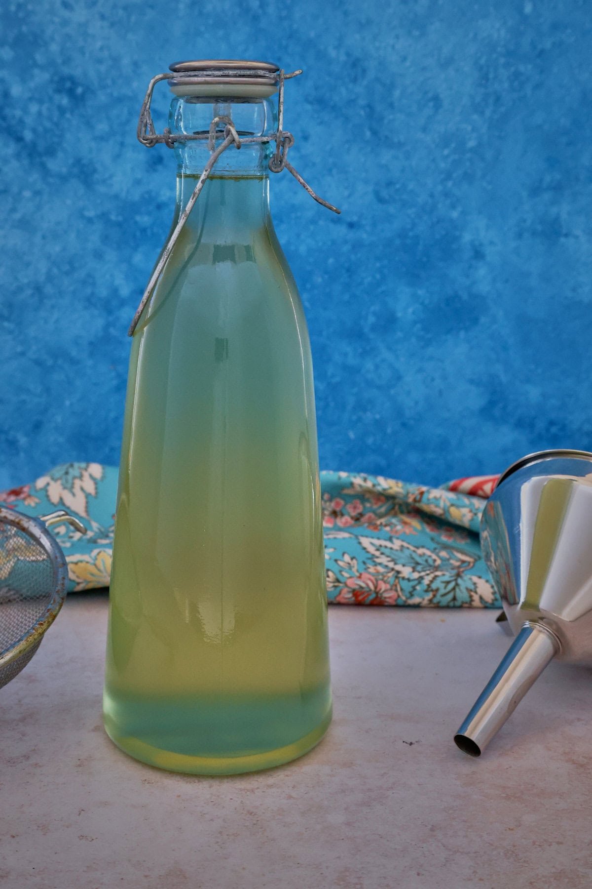 ginger syrup in a bottle with a strainer, kitchen towel, and funnel