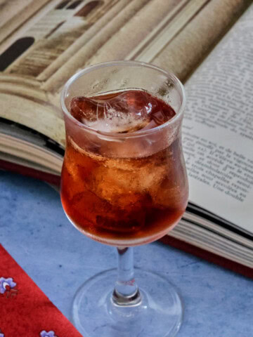 A glass of liqueur and glasses on a table next to an open book