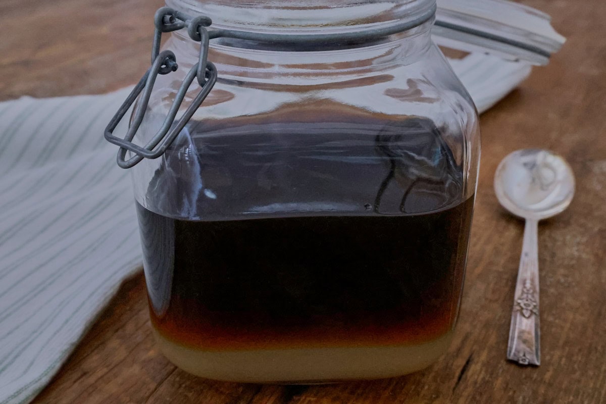 sugar and liqueur in a jar on a table with a kitchen towel and spoon alongside