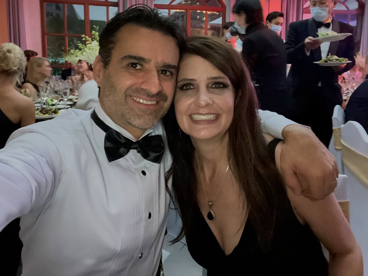 a couple in formal attire at a restaurant with diners and waiters in the background