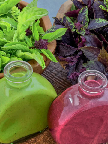 green and purple basil vinaigrette in small bottles, leaves of basil in bowls, and a napkin