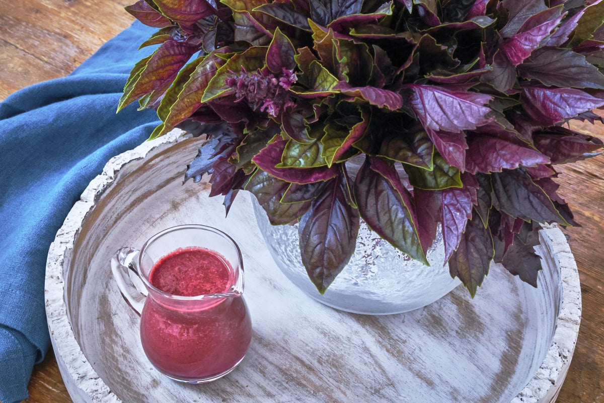 purple basil vinaigrette in a small pitcher on a tray along with a vase of purple basil leaves and a napkin alongside
