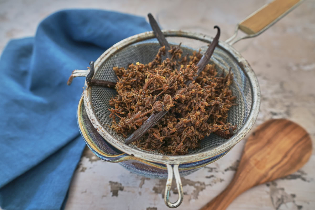 a mixing bowl with a strainer full of steeped lavender and vanilla beans, napkin, and mixing spoon