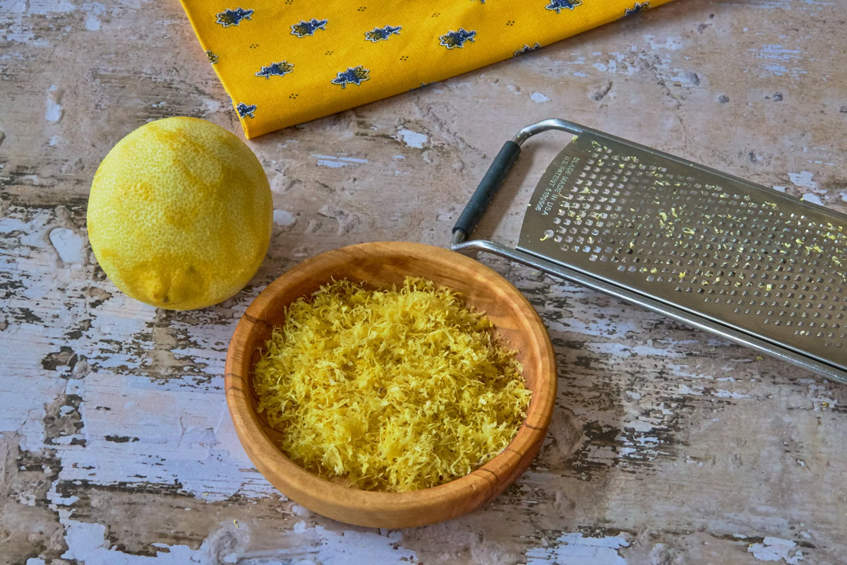 a zested lemon, napkin, bowl of lemon zest, and grater