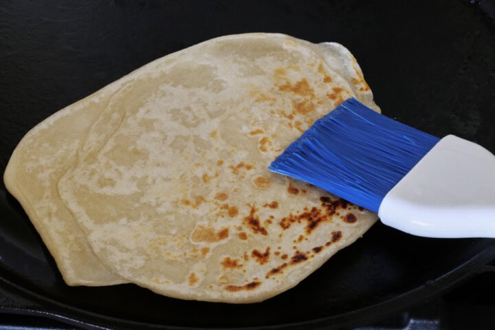 a browned flatbread on a skillet with a kitchen brush