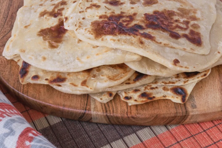 a stack of flatbreads on a wooden board with a table runner and kitchen towel