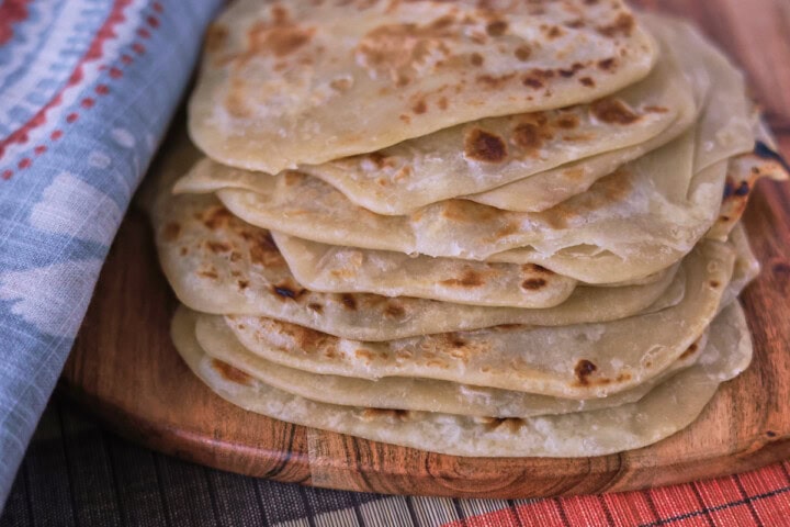 a stack of flatbreads on a wooden board with a table runner and kitchen towel