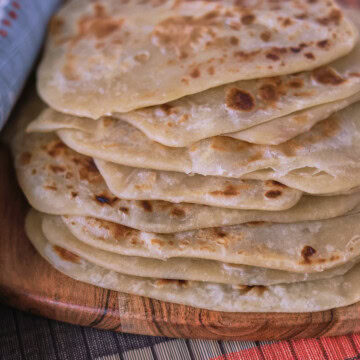 a stack of farata flatbreads on a wooden board with a table runner and kitchen towel