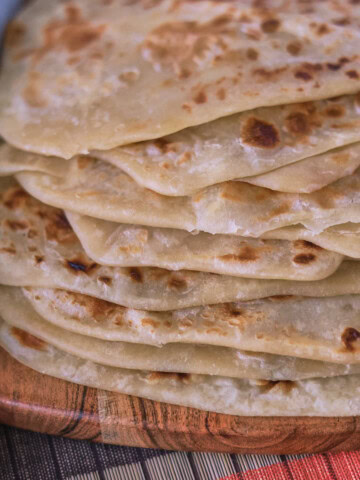 a stack of farata flatbreads on a wooden board with a table runner and kitchen towel