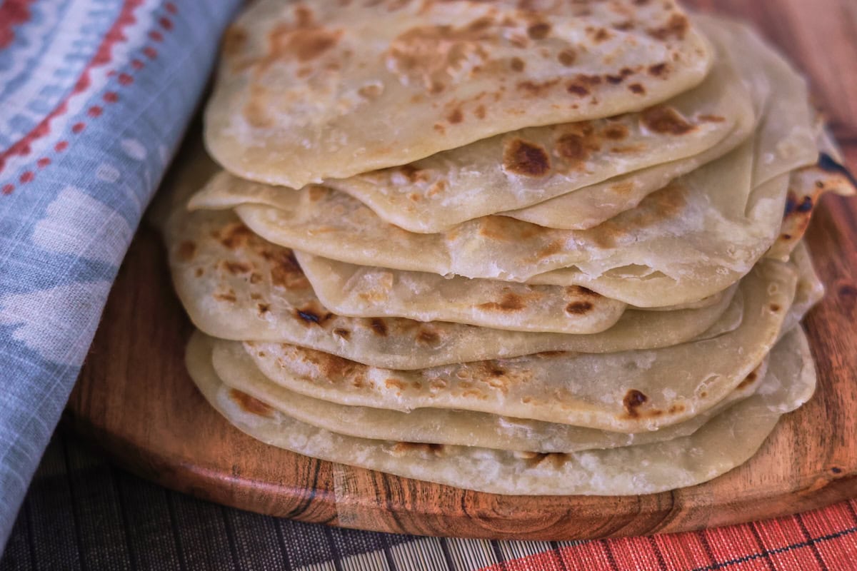 a stack of flatbreads on a wooden board with a table runner and kitchen towel