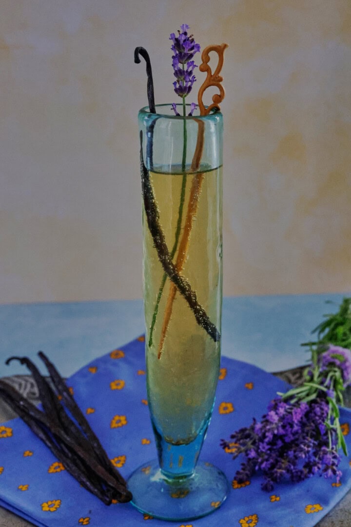 a cocktail in a champagne glass with a napkin, vanilla beans, and fresh lavender sprigs on a metal tray