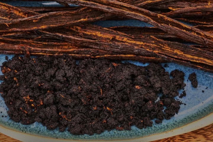 split vanilla beans and the seeds scraped from them on a plate on a wooden board
