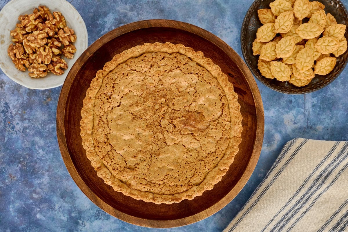 a walnut tart on a cake stand with plates of walnuts and cutouts and a kitchen towel