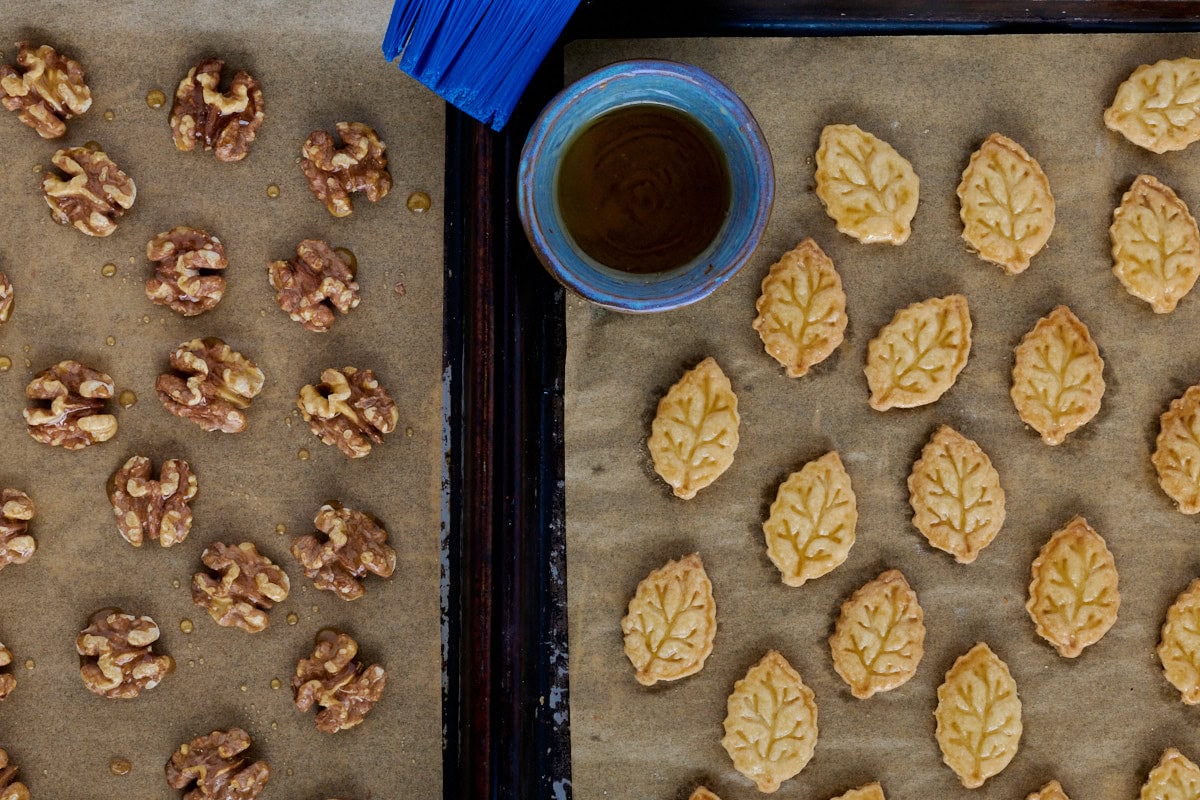 maple glazed walnuts and pie crust cutouts on parchment paper on cookie sheets with a bowl of maple syrup and a plastic basting brush