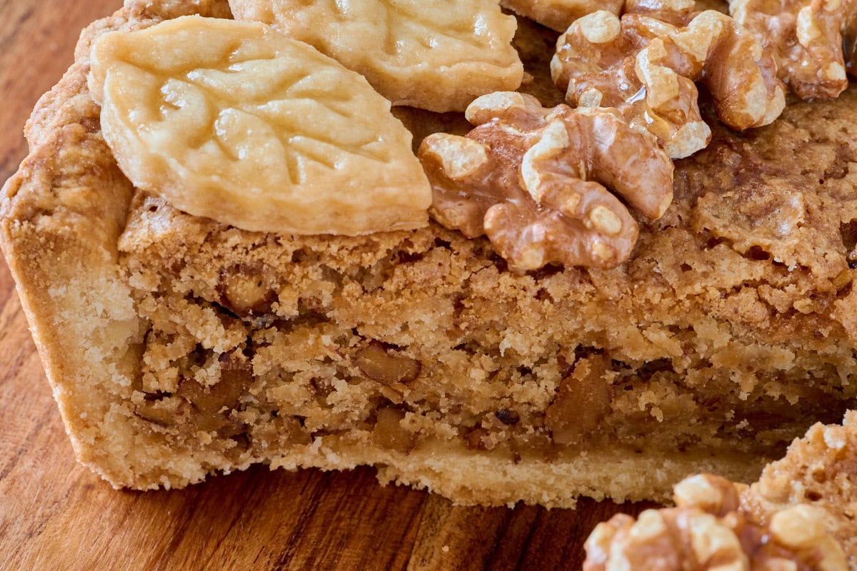 a closeup shot of a walnut tart with a removed slice on a cutting board
