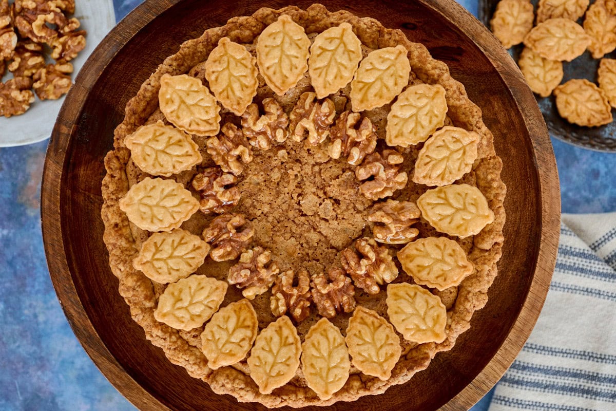 a walnut tart on a cake stand with plates of cutouts and walnuts and a kitchen towel