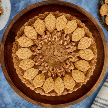 a walnut tart on a cake stand with plates of cutouts and walnuts and a kitchen towel in the background