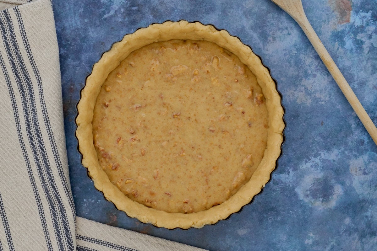 a filled tart crust, kitchen towel and wooden spoon